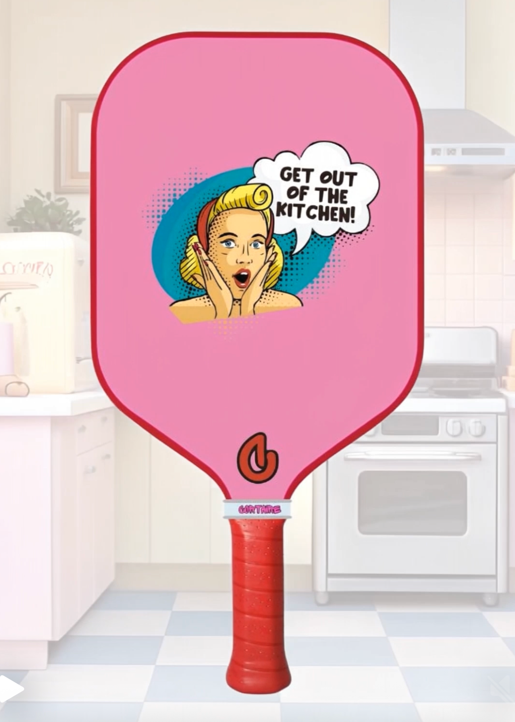 Pink pickleball paddle with a graphic of a pin up girl woman and text in a kitchen setting